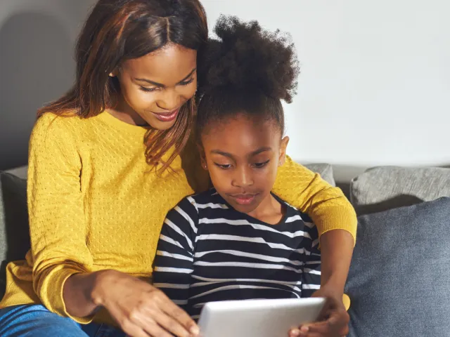 Une femme et sa fille utilisant une tablette dans leur canapé.